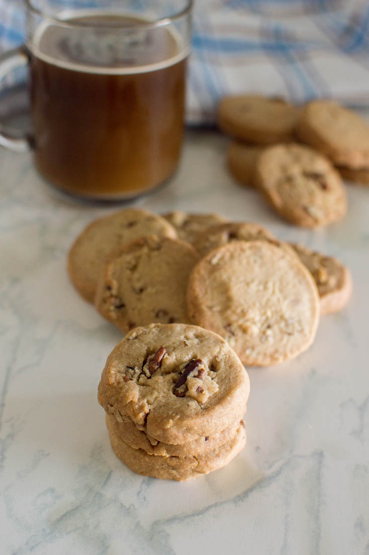 A stack of pecan shortbread cookies with more in the background as well as a glass mug of coffee