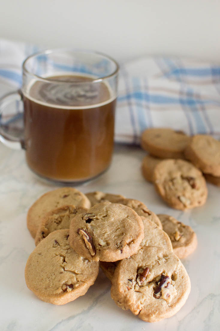 A pile of pecan shortbread cookies, made from scratch, with a cup of coffee in the background, adorned with a blue plaid napkin
