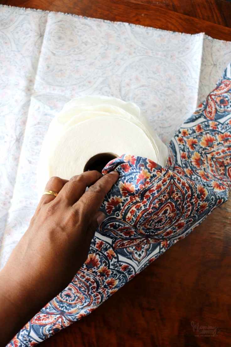 Blue and orange fabric being tucked into the center of the toilet paper roll.