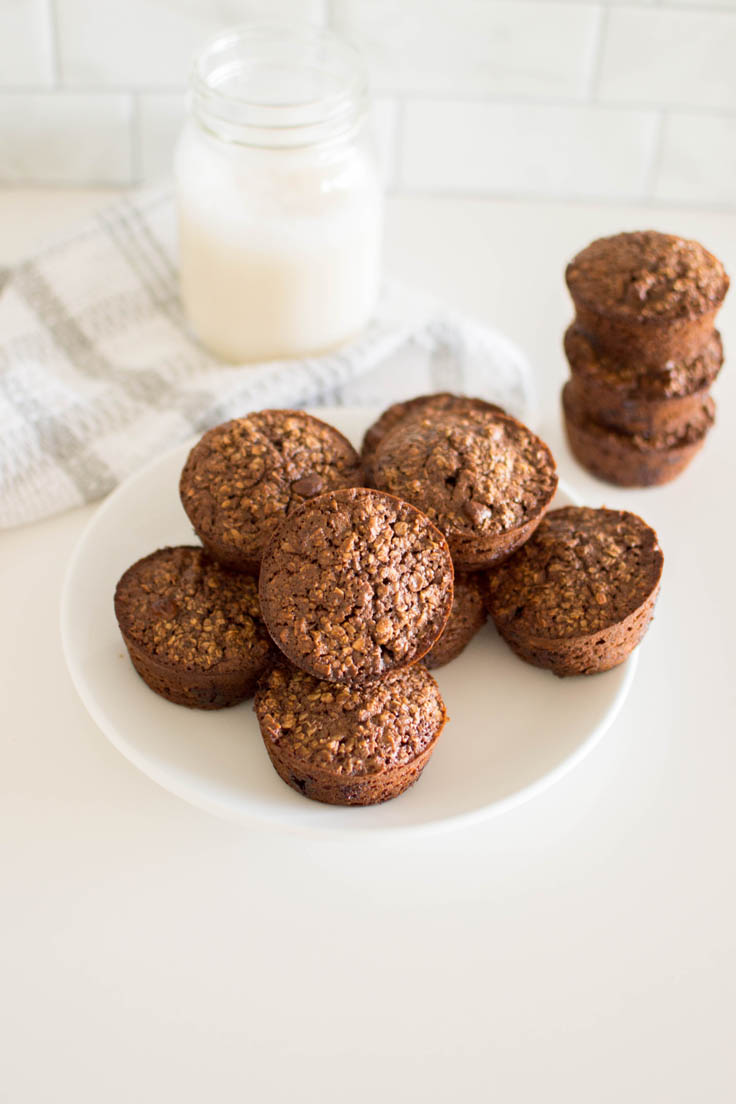 Baked Double Chocolate Oatmeal Cups on a white plate with a glass of milk and a plaid napkin in the background