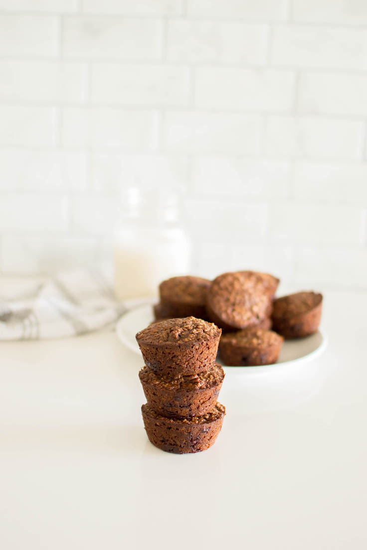 Three baked chocolate oatmeal cups stacked on top of each other with a plate of them in the background