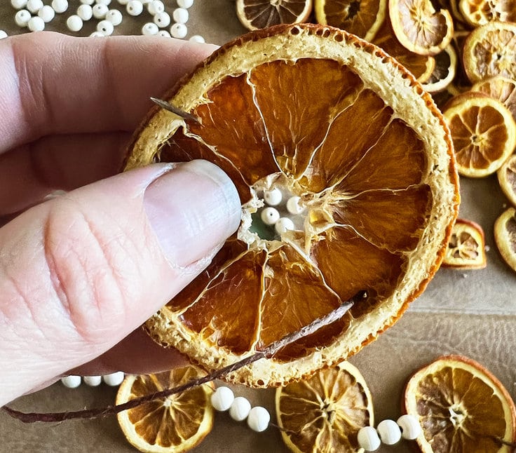 Using a needle to thread dried orange slices onto a garland