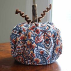 Blue and orange fall home decor- a blue and orange fabric toilet paper roll pumpkin on a wood table