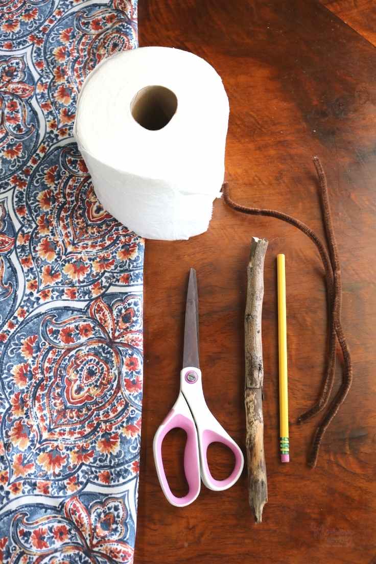 Large Toilet Paper Roll Blue and Orange Fabric, Fabric Scissors, Wood Stump, 2 Brown Pipe Cleaners, a Pencil