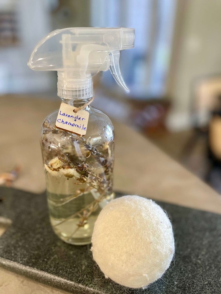 Close up a bottle of DIY Lavender and Chamomile room spray next to a wool dryer ball.