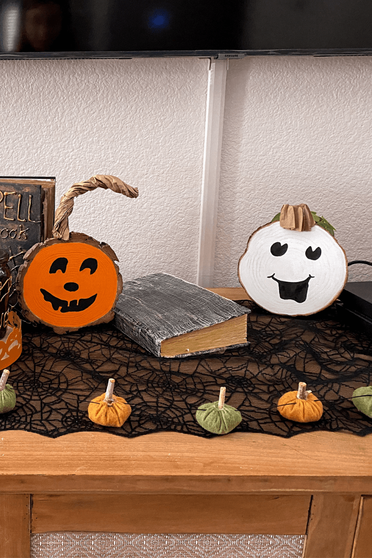 One orange pumpkin with a happy face on the left and a white pumpkin with a happy face on the right with a book in between and pumpkin garland in front.