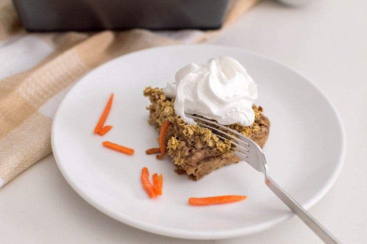 A fork slices into a piece of carrot cake oatmeal bake on a white plate, surrounded by shredded carrots