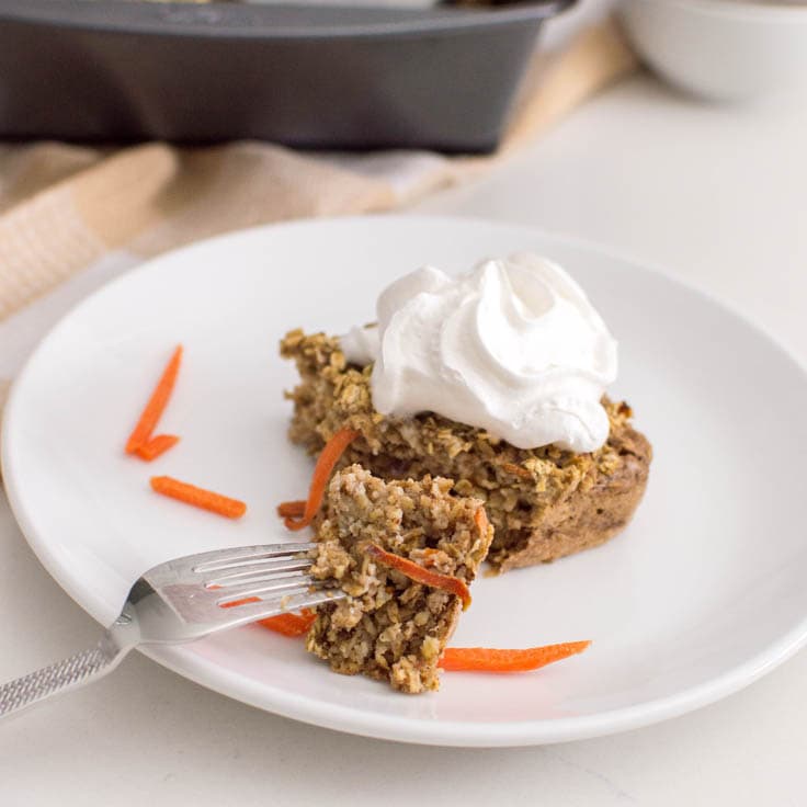 A fork on a white plate, with a piece of carrot cake oatmeal bake and a larger slice behind it