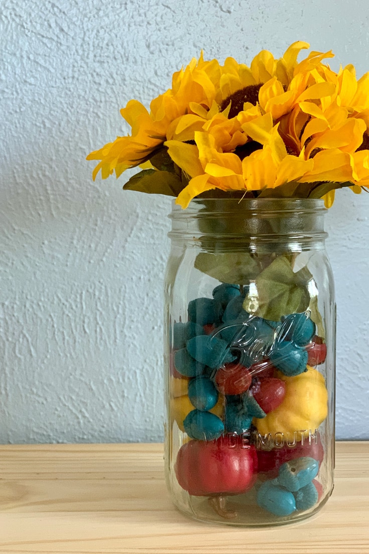 A Ball canning jar filled with blue, red, and yellow acorns and mini pumpkins and silk sunflowers.