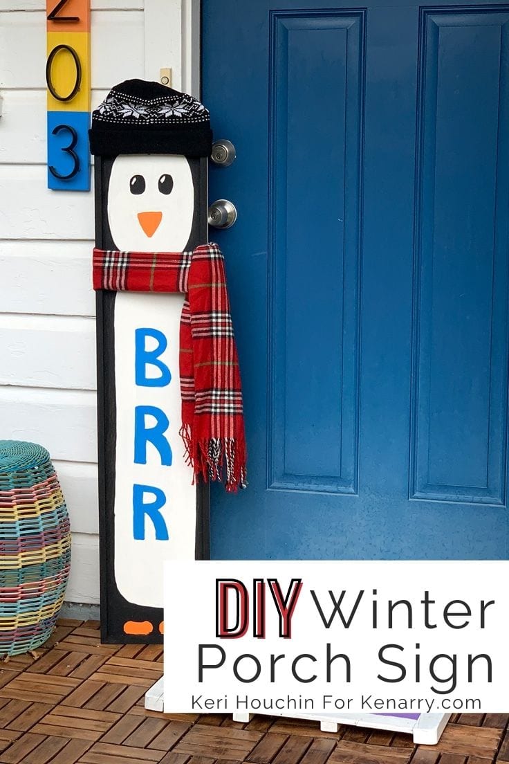 DIY winter porch sign made from a board painted to resemble a penguin wearing a real hat and scarf.