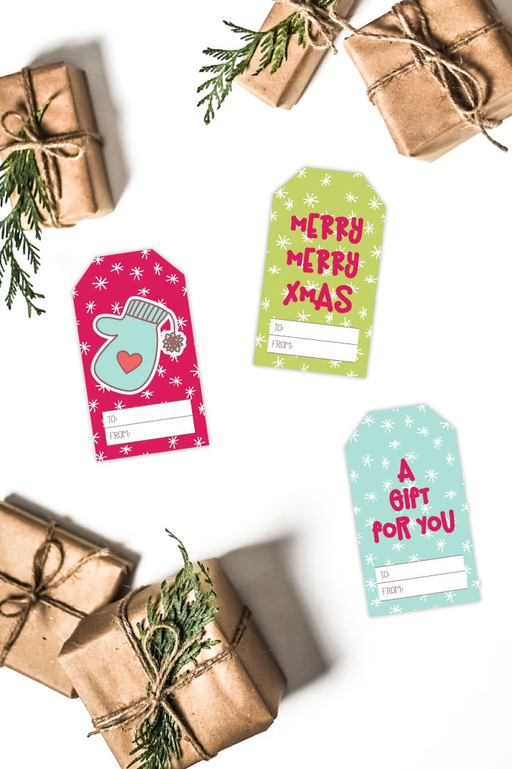 Preview of three tags cut out from freebie Christmas tag pdf on a white background with golden kraft paper wrapped gifts scattered on top and bottom left corner. 