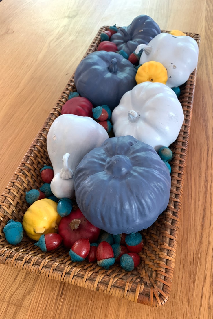 A long basket filled with blue, red, and yellow painted pumpkins and acorns.