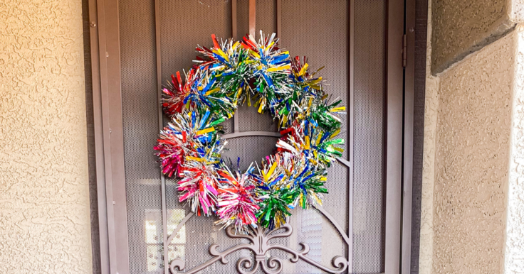 multi colored tinsel garland pool noodle wreath hanging on a brown screen door