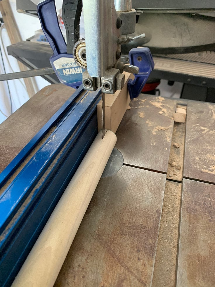 a band saw with the fence aligning the blad to cut the center of the ladder rung or wood dowel and a wood stop is clamped along the saw fence to keep the blade from going to far into the edge of the dowel. 