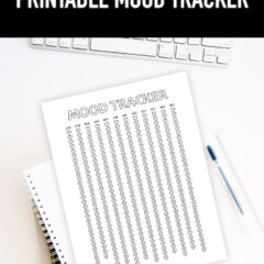 Preview of mood tracker printable on desk with keyboard on top and stack of notebooks and a pen.