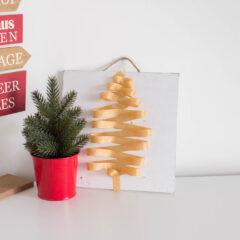 Our very own holiday-themed door hanger sitting on a white table with other Christmas decor
