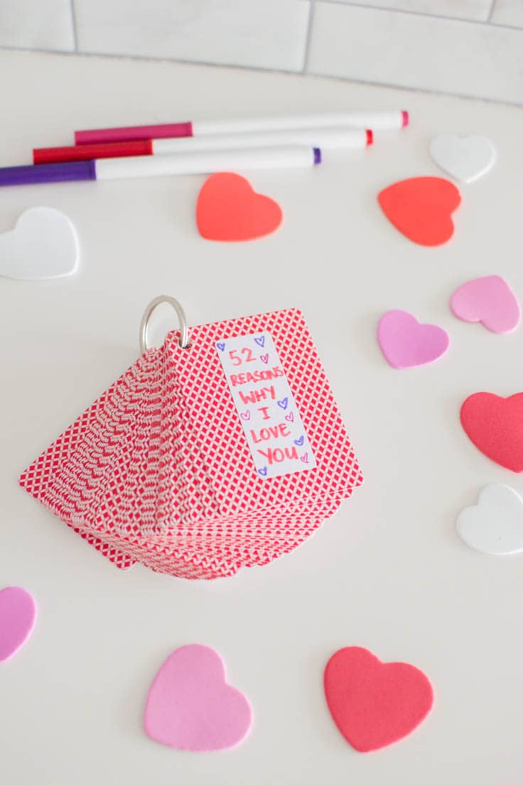 A deck of playing cards, held together by a keyring, laying on a white table, surrounded by confetti hearts and markers