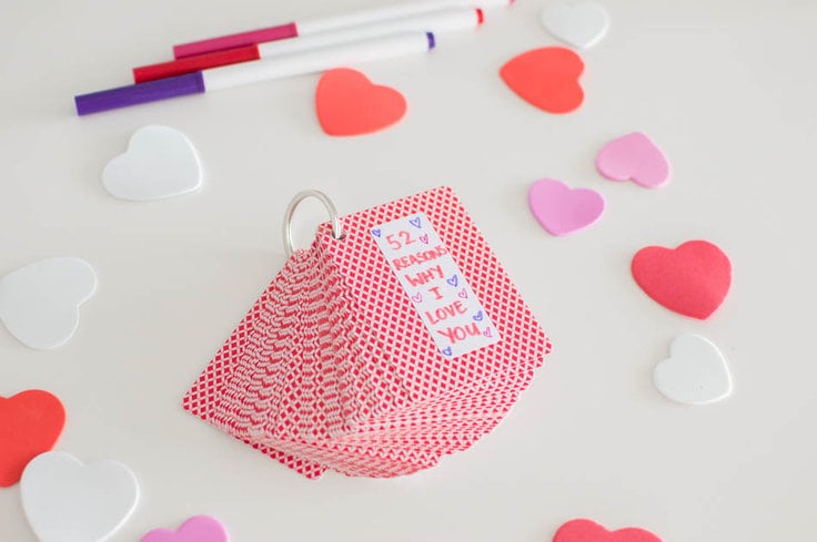 A deck of playing cards, held together by a keyring, laying on a white table, surrounded by confetti hearts and markers