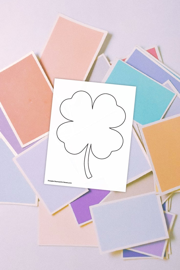 Preview of four leaf shamrock shape on top of scattered stack of pastel colored papers. 
