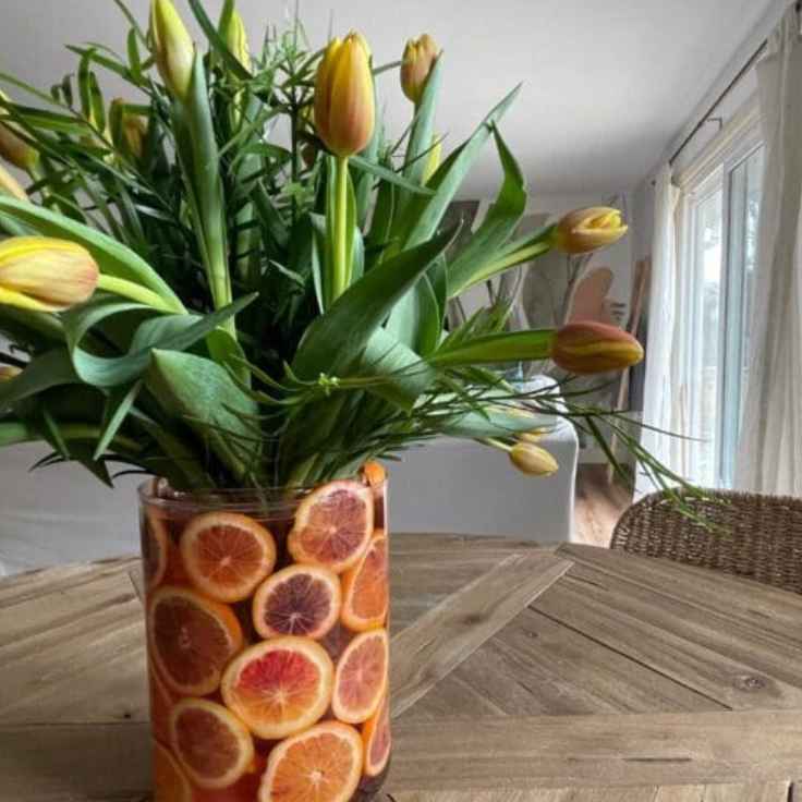 A vase of tulips with orange slices around the edges