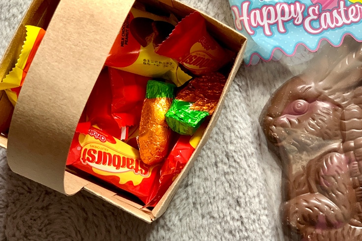Overhead view of chocolate bunny beside a basket of Starbursts, peanut butter eggs, and chocolate carrots.