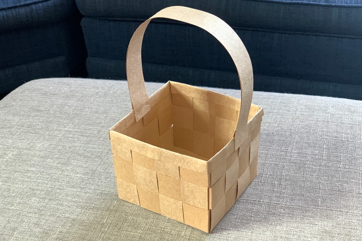 Empty kraft paper basket woven with 3 rows of paper and a handle glued in the center.