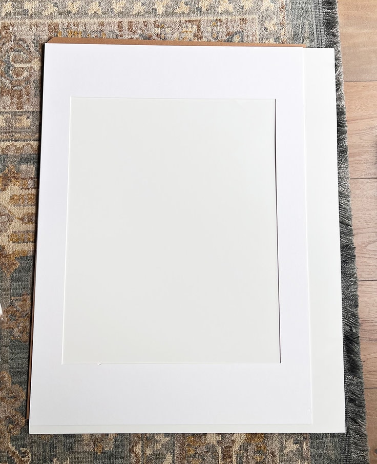 the picture frame mat is placed on top of the poster board and used as a template to cut the poster board in order to fit in the picture frame.