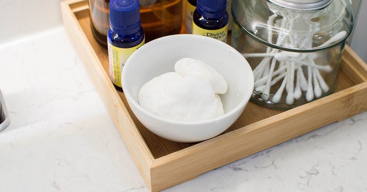 A small white bowl filled with DIY shower steamers, surrounded by other bathroom items like essential oils, a jar of Q-tips, etc.