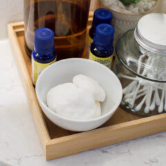 A small white bowl filled with DIY shower steamers, surrounded by other bathroom items like essential oils, a jar of Q-tips, etc.