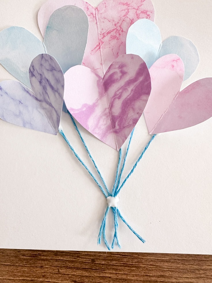 Multiple color hearts on a white card with blue strings attached to them