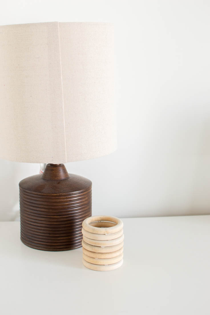 A DIY Wood Vase made of macrame wood rings, sitting next to a wooden lamp