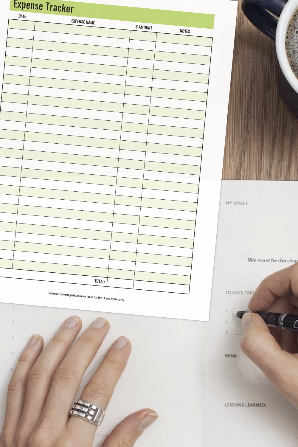 Preview of expense tracker printable on a wooden desk background with partial view of coffee mug in upper right hand corner with hands filling out a planner notebook underneath. 