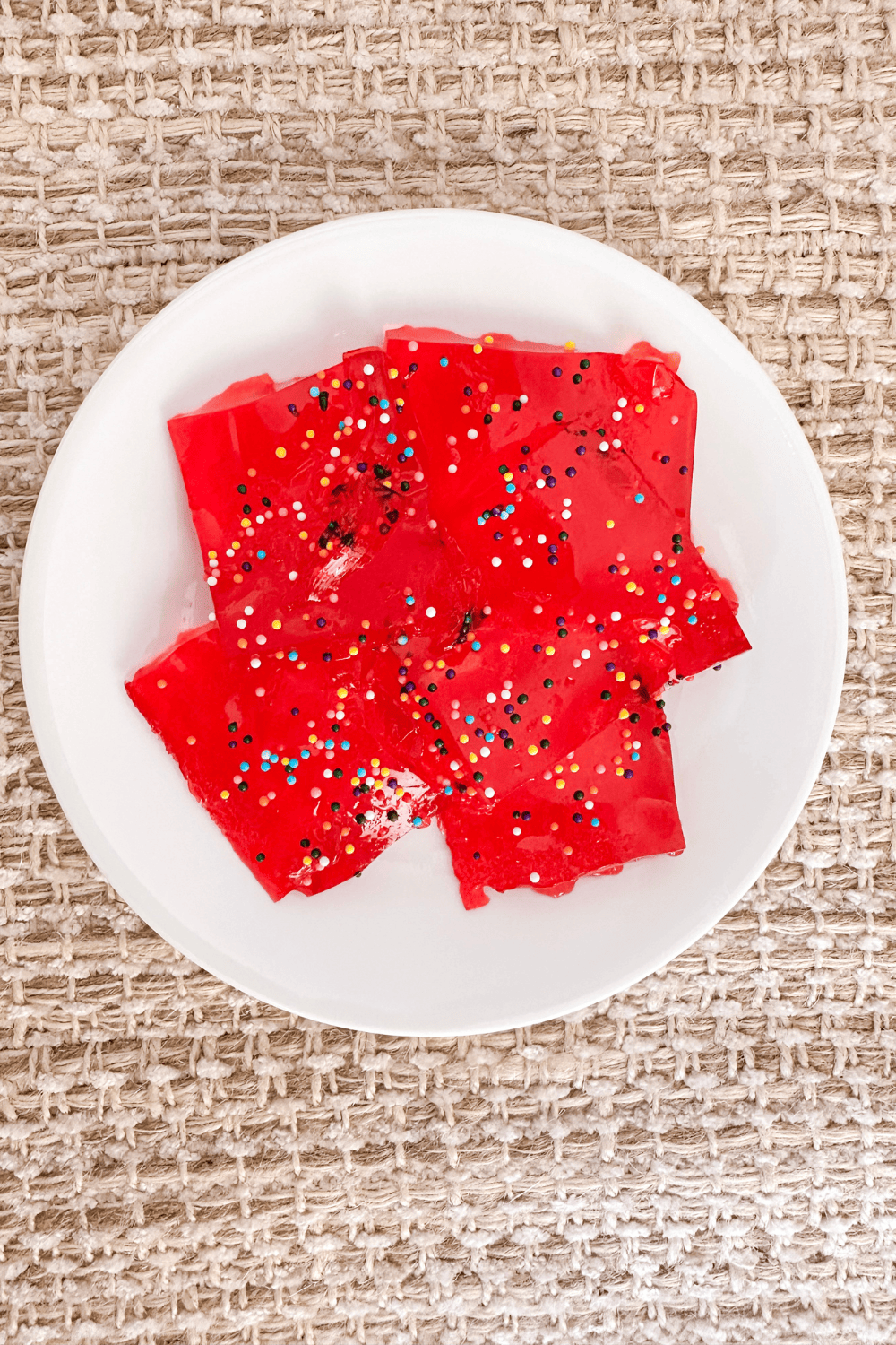 Red jello with rainbow sprinkles on a white plate