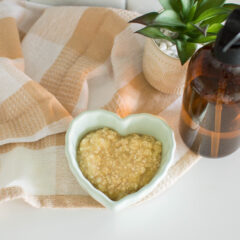 Bananas, oats, and honey mashed and mixed together to create a homemade face mask, in a heart-shaped bowl, sitting on a plaid tea towel