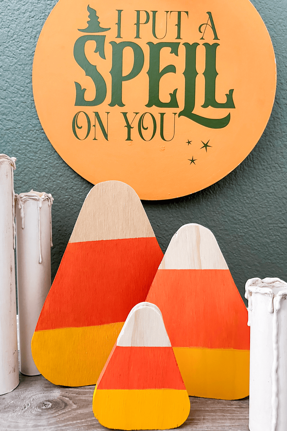 3 wooden candy corn with dripping candles on either side in front of a green wall with a picture that says 'I put a spell on you' hanging on it.