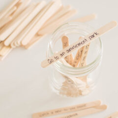 A popsicle stick with writing propped on the top of an open mason jar