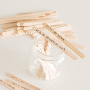 Two popsicle sticks with writing propped on the top of an open mason jar