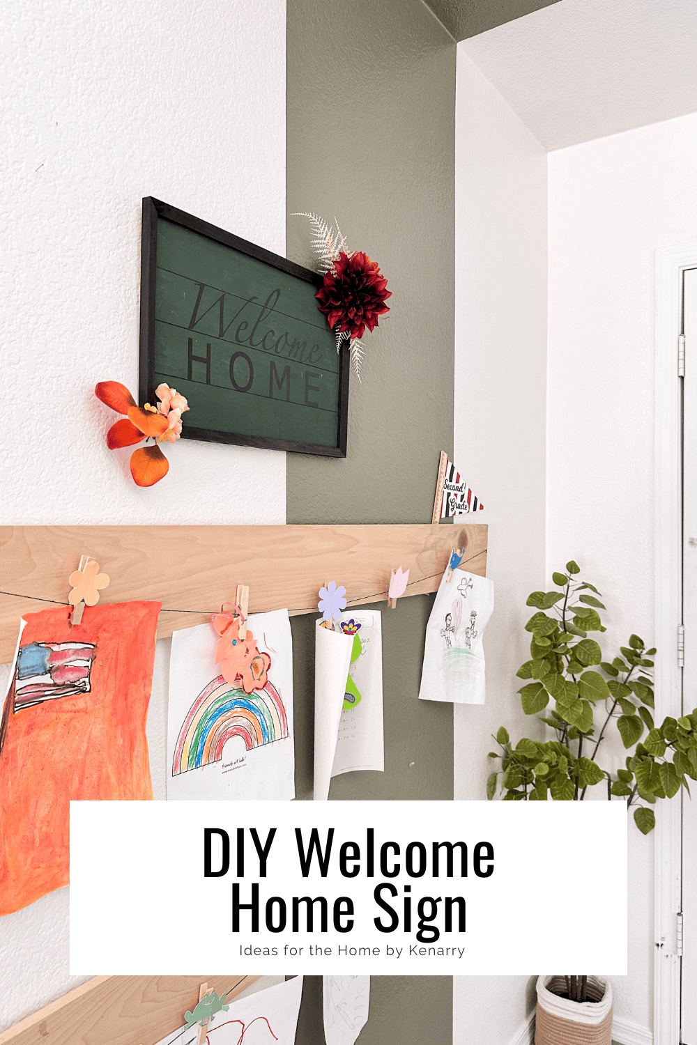 Green sign with a black frame that says Welcome Home with burgundy and burnt orange flowers hanging on a white and green wall with artwork hanging below it