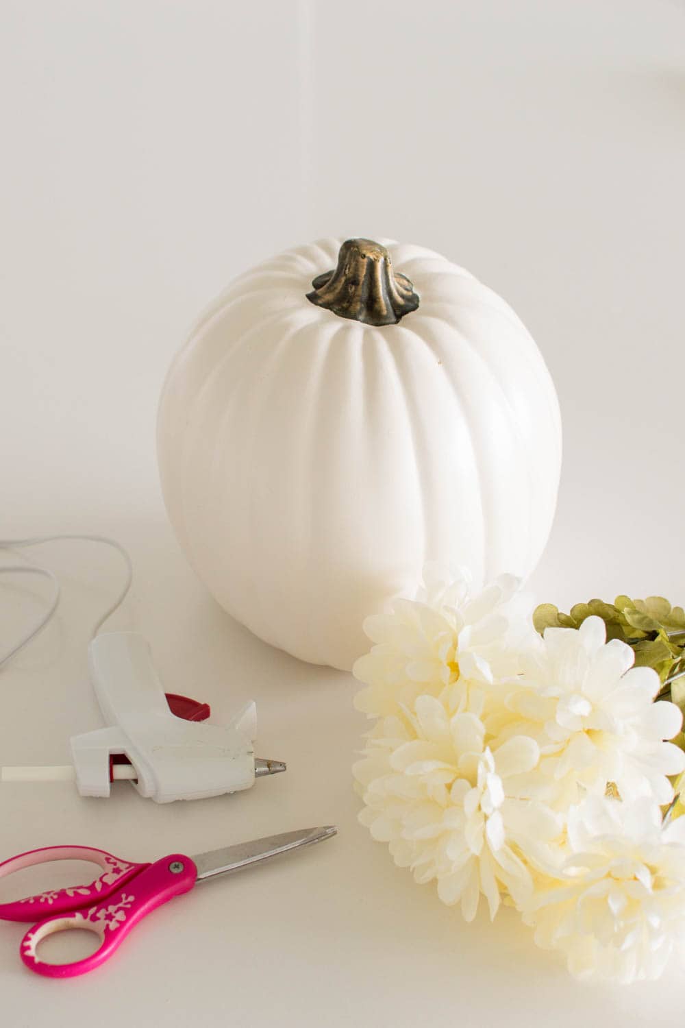 Required supplies including a white plastic pumpkin and a hot glue gun to create a DIY White Pumpkin Centerpiece
