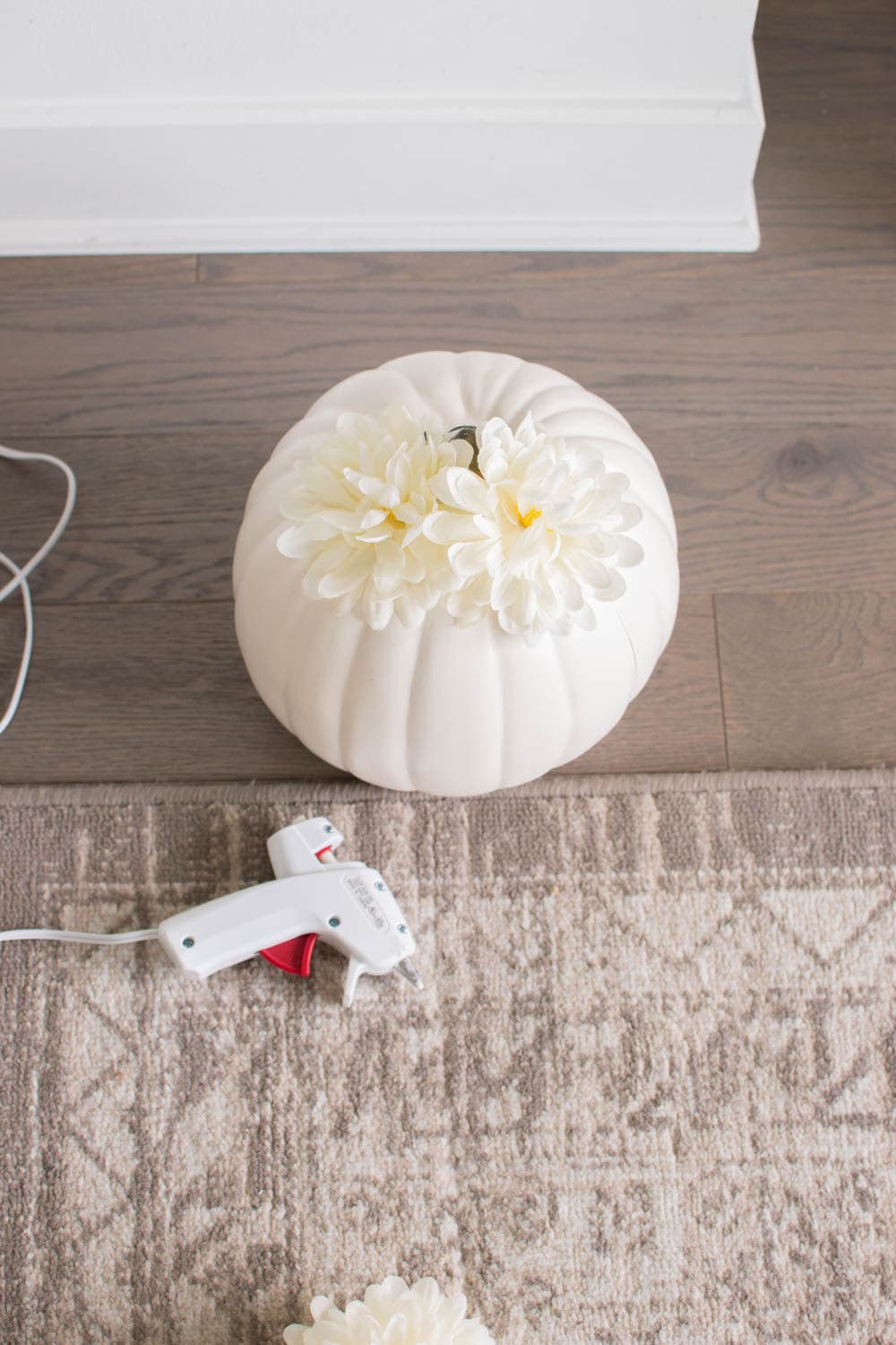 Gluing faux flower buds on a white plastic pumpkin