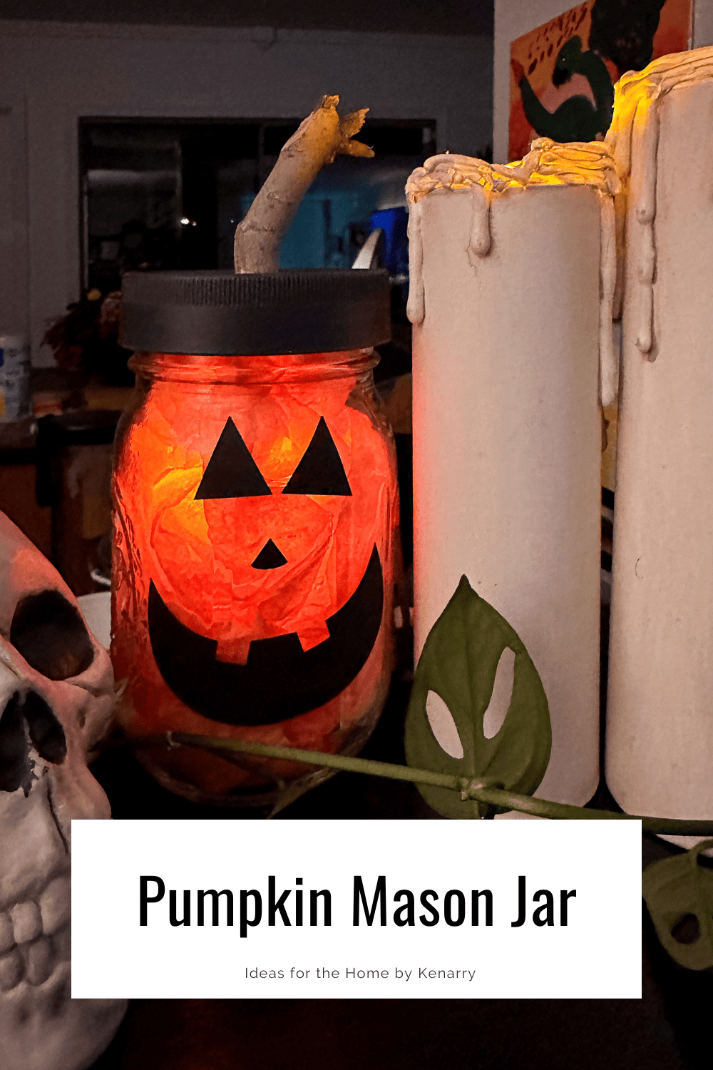 Mason Jar pumpkin sitting next to candles and a skull with a plant in front.