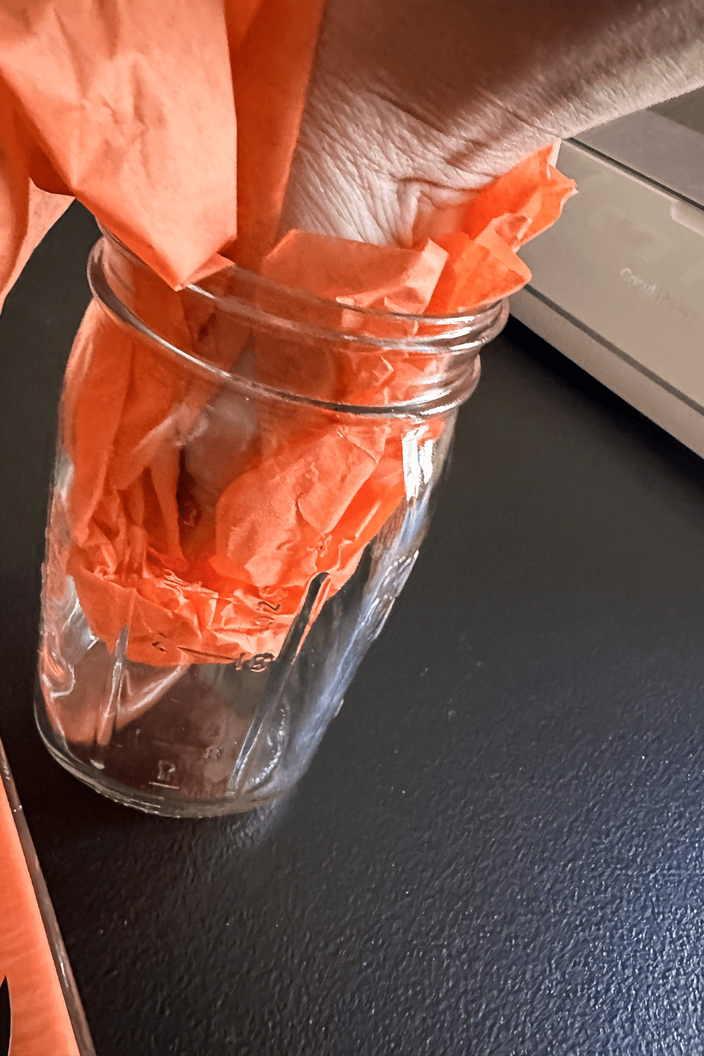 a hand pushing orange tissue paper into a mason jar