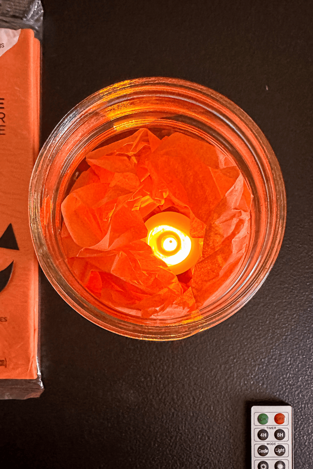 top view of orange tissue paper in a mason jar with a candle sitting in the center of the tissue paper.
