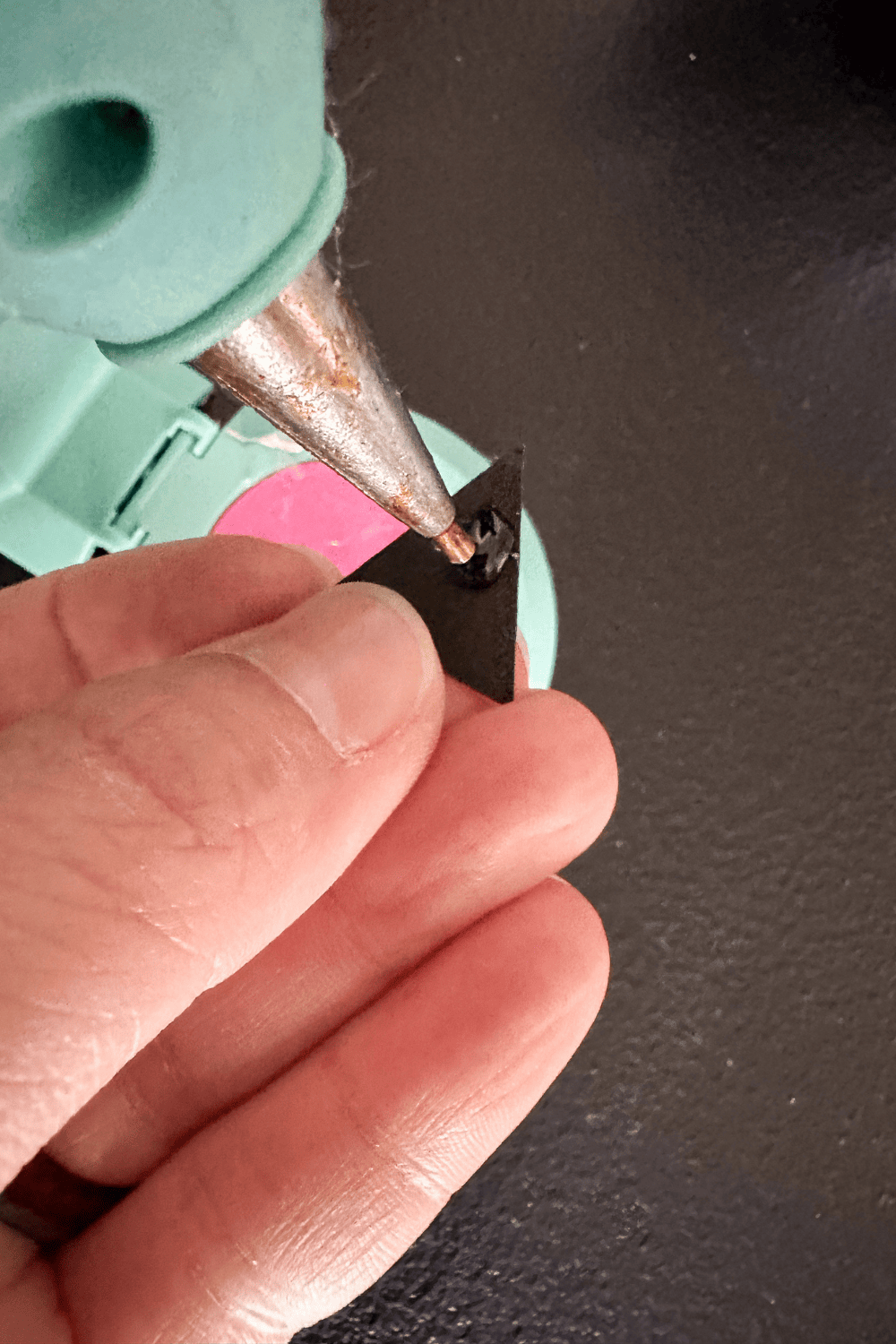 hand holding a tiny triangle of black cardstock up to a hot glue gun