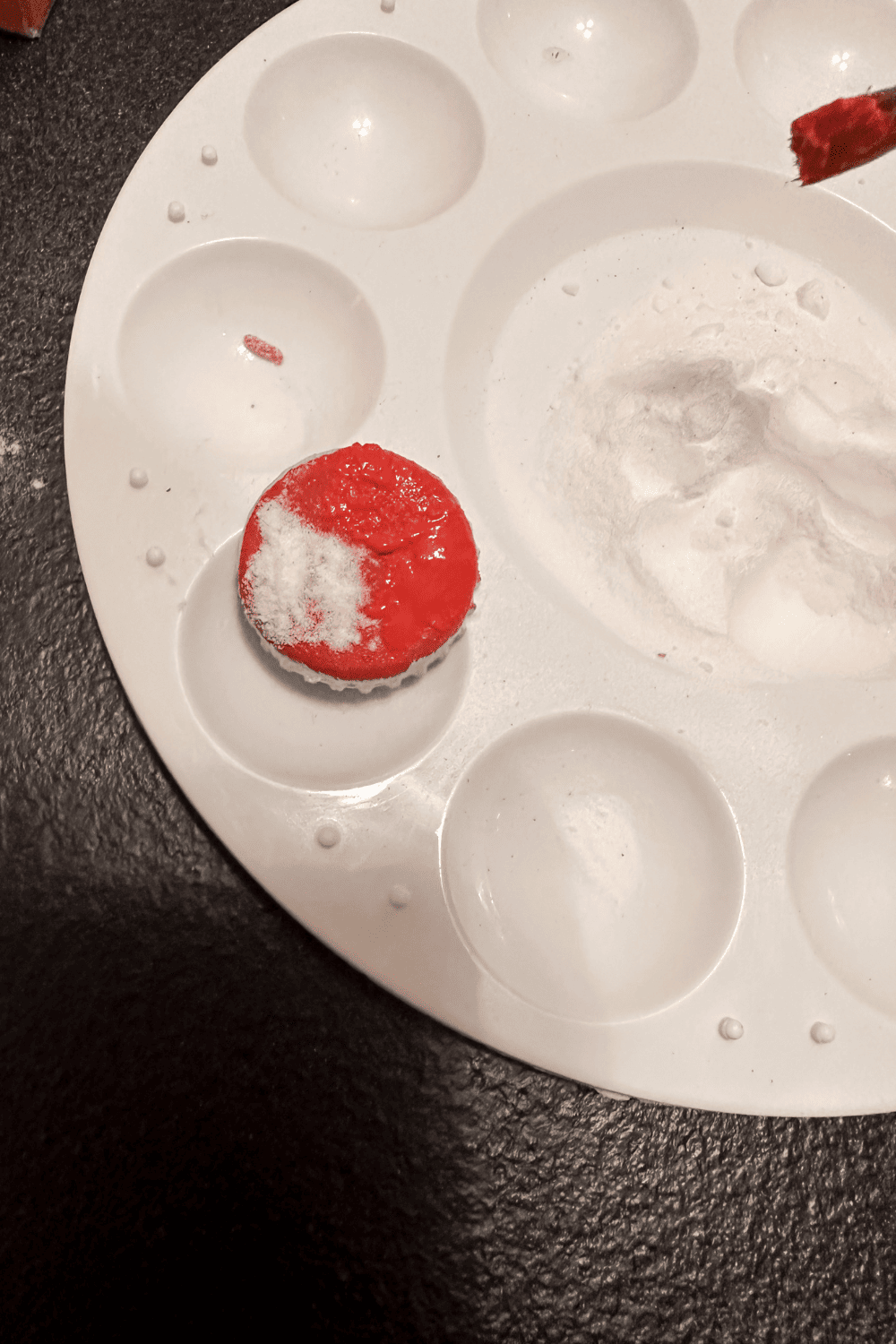 bottle cap painted red with baking soda sprinkled on top and paint being reapplied