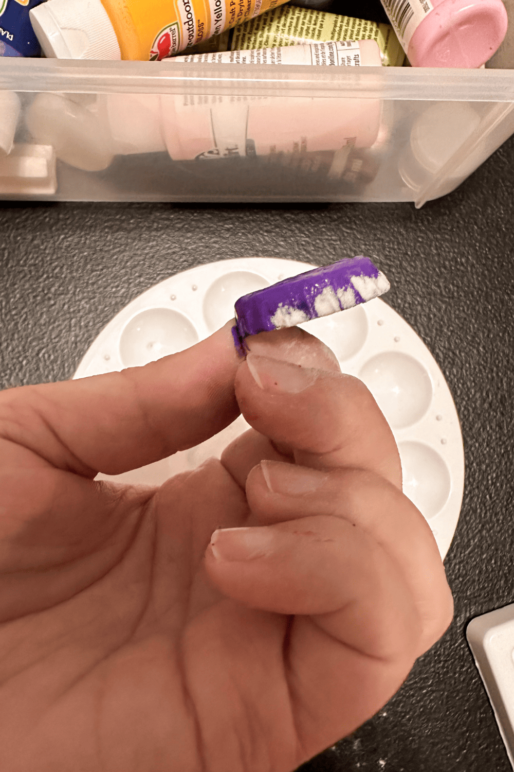 hand holding a bottle cap painted purple with baking soda on the edge
