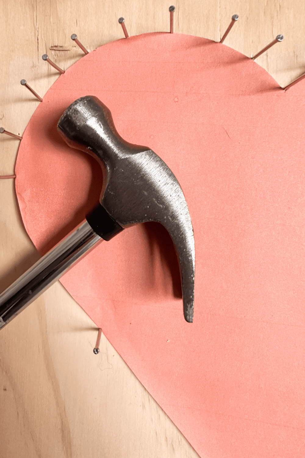 A paper heart with nails surrounding it, a hammer in the center