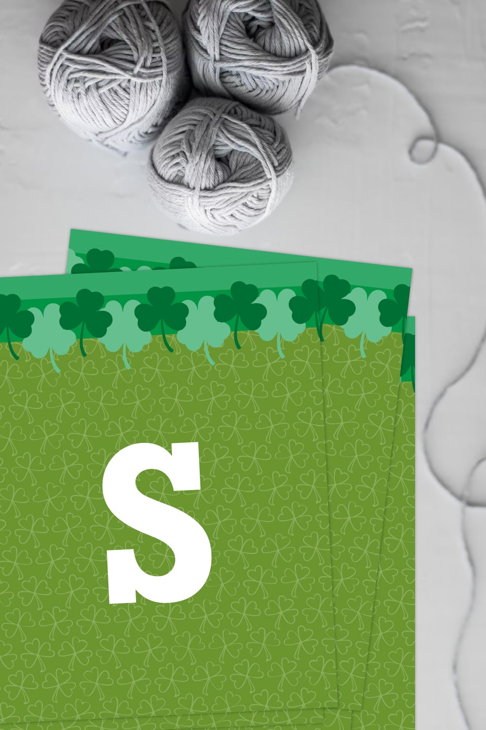 Preview of a few green printable pages of st patrick's day banner on white background with 3 rolls of gray yarn on the top left. 