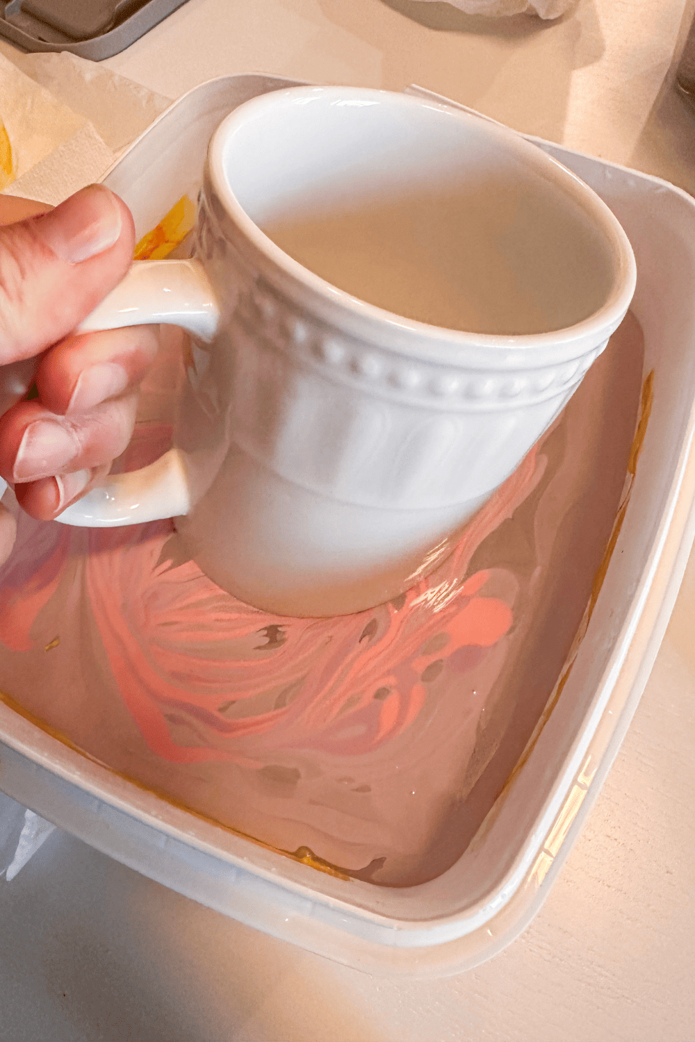 a mug being dipped into purple and pink nail polish swirled on top of water