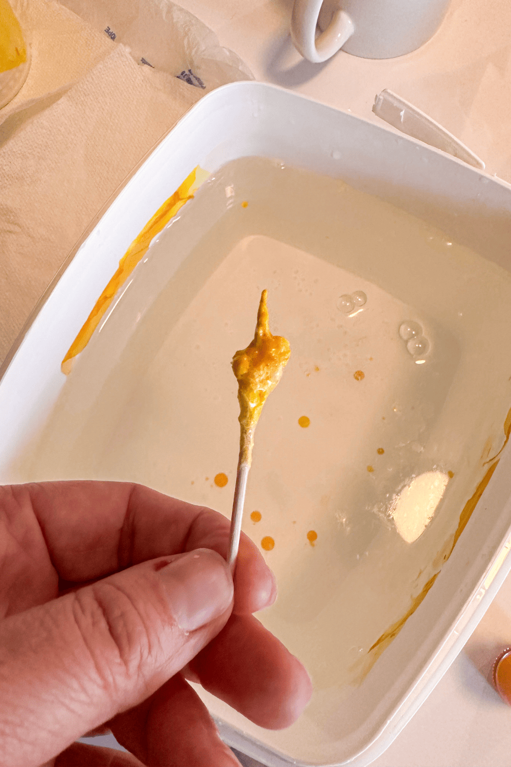 yellow dried nail polish on a toothpick with a container of water in the background